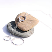 Silver necklace featuring two smaller hoops and one larger hoop. The necklace is looped through a smaller hoop. The other two hoops are attached to the hoop with a jump ring. This holds two short bits of chain in place to which the two hoops are attached.