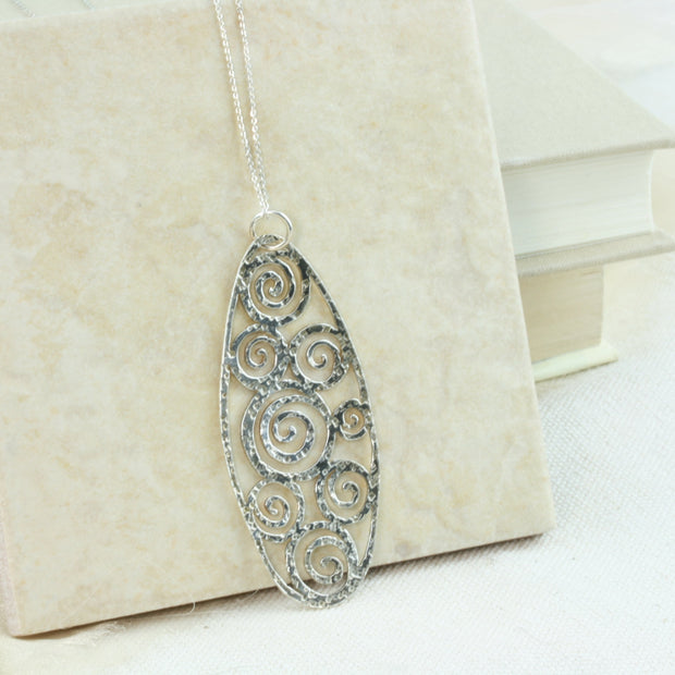 A large oval pendant necklace featuring 8 different sizes swirls all around the inside of the oval frame. It has a round hammered texture and a shiny finish which captures and reflects the light to make the necklace sparkle.