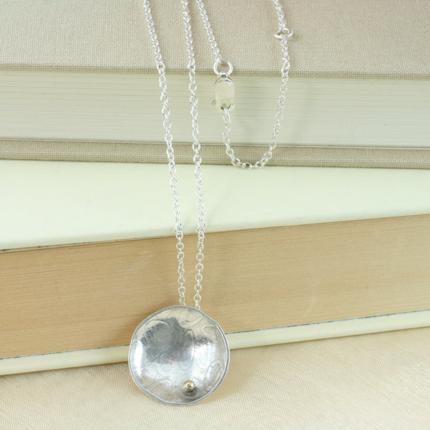 Eco silver pendant necklace with a pebble texture and mirror finish. Featuring a gold ball on the inside at the bottom half of the cup.