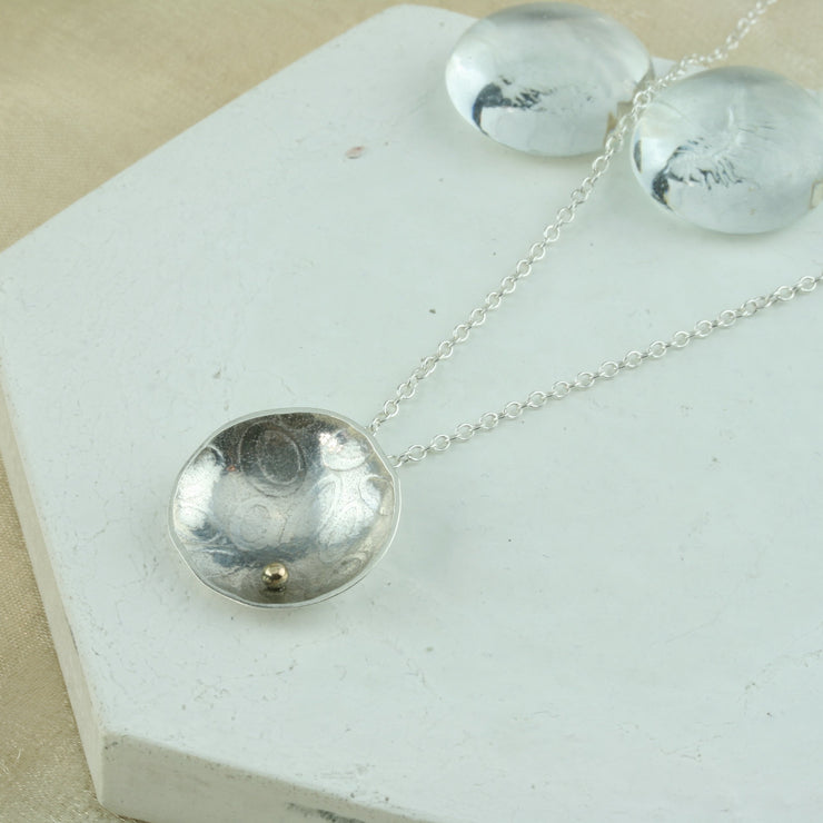 Eco silver pendant necklace with a pebble texture and mirror finish. Featuring a gold ball on the inside at the bottom half of the cup.