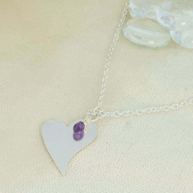 Silver personalised pendant necklace with a large heart shaped pendant that can be personalised with a word, name, initials or symbols of your choosing. The pendant can be fastened at various lengths. The pendant is made using eco silver. This version shows the pendant necklace with the addition of an Amethyst gemstone, more gemstones are available too.