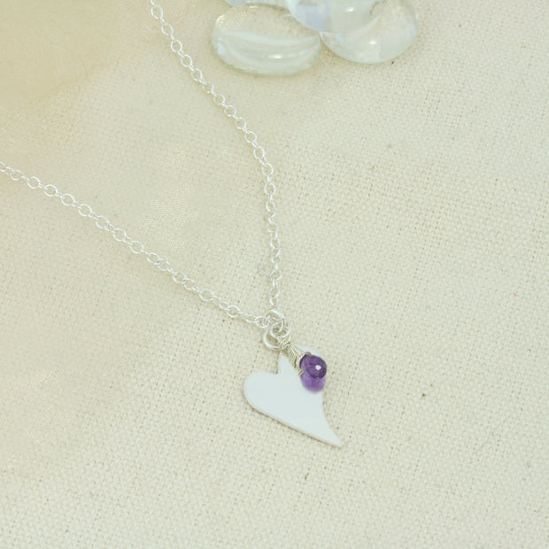 Silver personalised pendant necklace with a small heart shaped pendant that can be personalised with a word, name, initials or symbols of your choosing. The pendant can be fastened at various lengths. The pendant is made using eco silver. This version shows the pendant necklace with the addition of an Amethyst gemstone, more gemstones are available too.