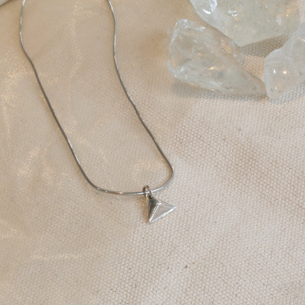 A silver pendant in the shape of a pyramid. IT has a mirror finish and comes with a snake chain necklace.