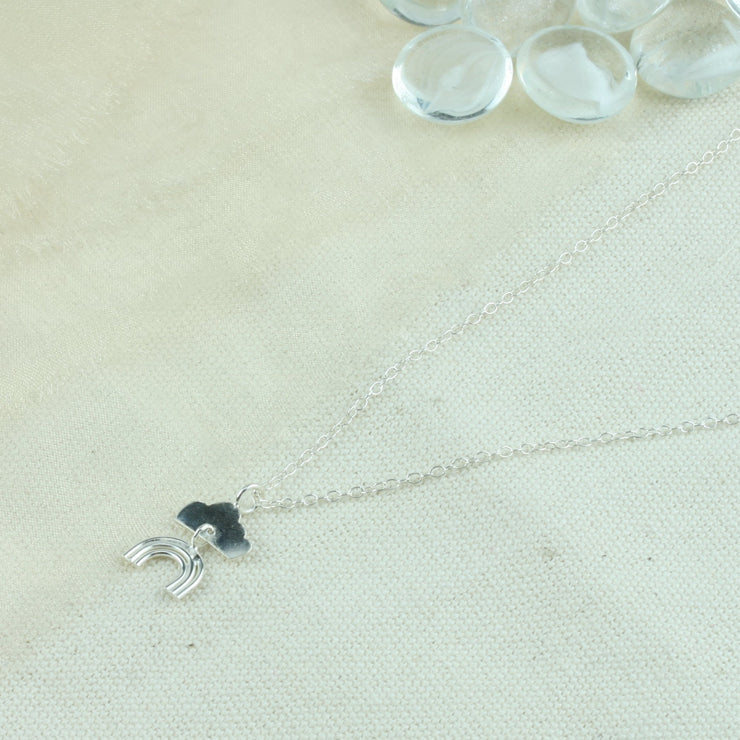 Eco silver pendant necklace featuring a cloud with a rainbow charm underneath it, attached with a jump ring. The necklace is adjustable and can be worn at two different lengths.