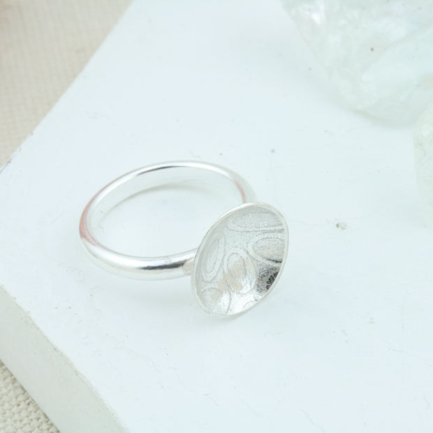 Eco silver cup ring with a silver ring band and a domed cup with a pebble texture. 