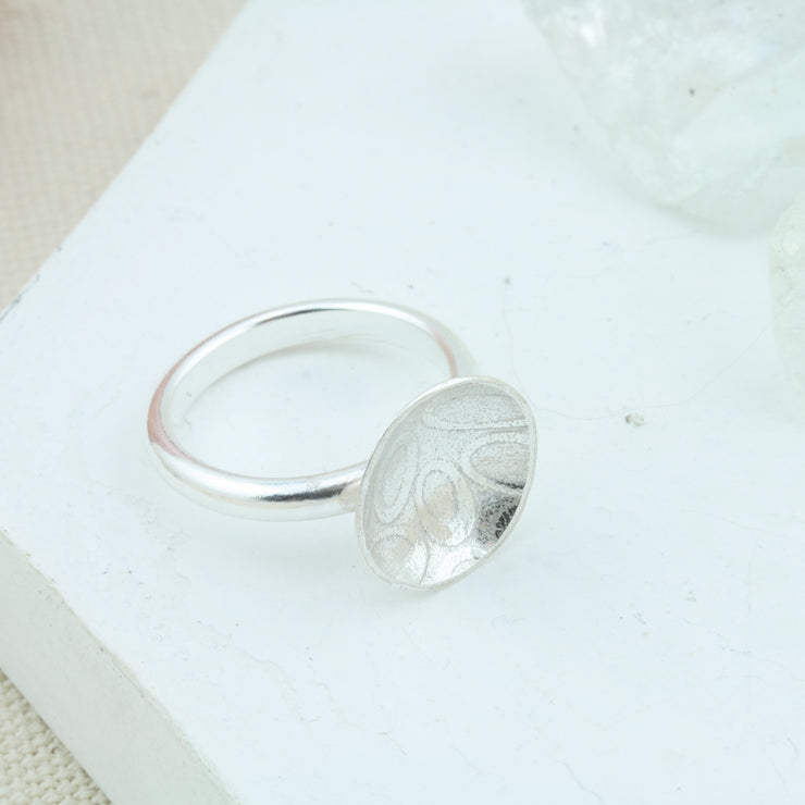 Eco silver cup ring with a silver ring band and a domed cup with a pebble texture. 