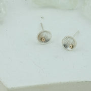 Eco silver domed cups with a pebble texture.  A 9ct gold ball sits a bit to the side at the bottom half of the cup. The earrings have a shiny finish.