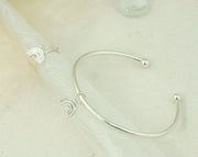 Eco silver bangle with a small rainbow charm. It is attached to the bangle with a jump ring, so it moves freely around the bangle. The bangle has a silver ball on each end and can be adjusted in width by pulling or pinching it gently. The rainbow features three arches made from round eco silver wire. The whole piece has a shiny mirror finish. Shown here with a matching adjustable ring with a rainbow charm.
