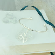 Silver bangle with a silver snowflake charm. The snowflake charm is attached with a jump ring and moves freely along the bangle. It has a hammered finish on one side and a mirror finish on the other. The ends of the bangle have a silver ball.