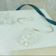 Silver bangle with a silver snowflake charm. The snowflake charm is attached with a jump ring and moves freely along the bangle. It has a hammered finish on one side and a mirror finish on the other. The ends of the bangle have a silver ball.