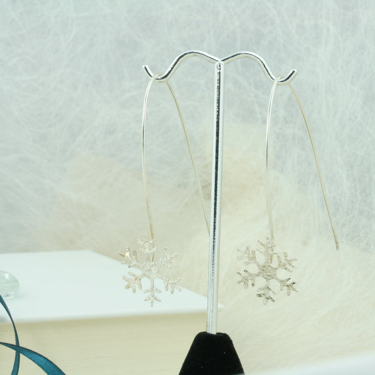 Silver earrings featuring a snowflake with a hammered shiny finish, which sparkles in the light. The snowflake is attached to the silver wire that loops through the ear and drops 5cm on both sides, showing off the snowflake perfectly.