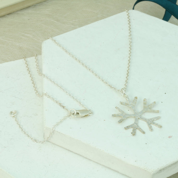 Silver snowflake pendant necklace with a hand sawn classic snowflake shape. IT has a hammered texture which gives it a shimmer when it captures the light, and a shiny finish.
