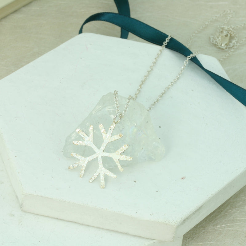 Silver snowflake pendant necklace with a hand sawn classic snowflake shape. IT has a hammered texture which gives it a shimmer when it captures the light, and a shiny finish.