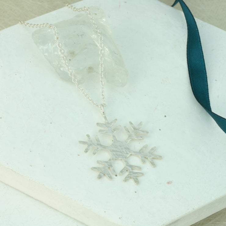 Silver pendant necklace featuring a snowflake with a hexagon in the heart. It has a hammered shiny finish which sparkles when it catches the light. The chain can be fastened at two different lengths making it versatile to match with any outfit.