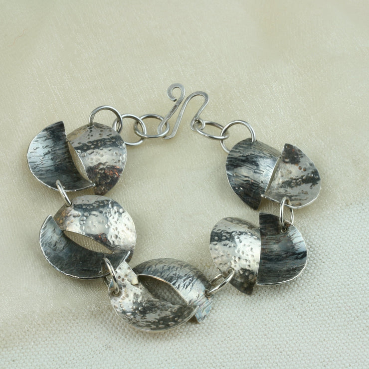 This handmade silver bracelet features 5 split circles and is 20cm long. The circles have been sawn in half, domed and soldered together in opposite directions.  They are approximately 2.5cm in diameter and have a hammered textured finish.  One half is oxidised and looks darker than the other.