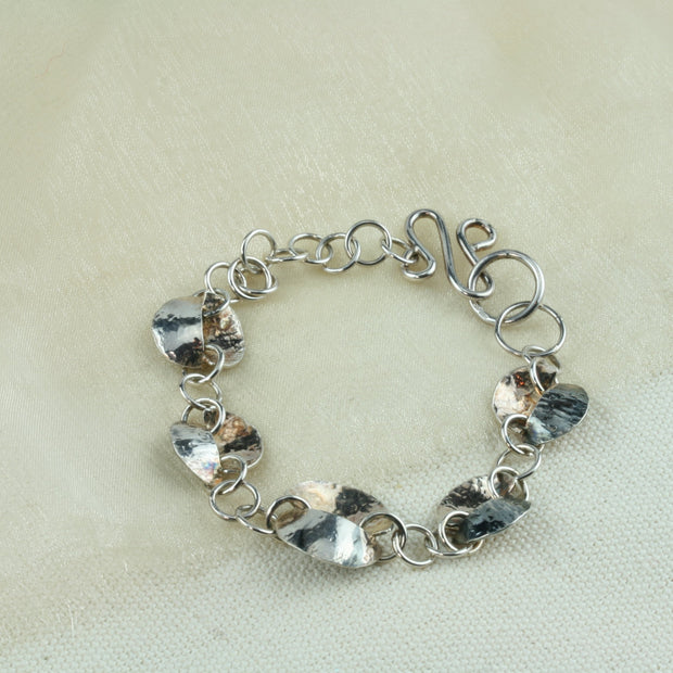 Silver bracelet featuring five split circles, four smaller and the middle one a bit larger. All connected by larger jump rings. The circles have been sawn in half and domed and soldered together in opposite directions. Both with a different texture. 