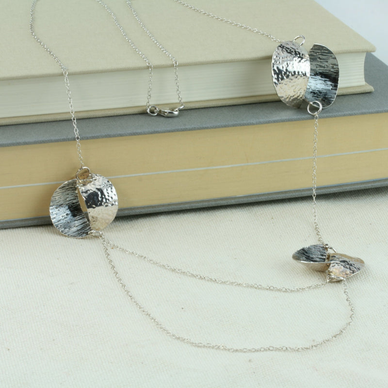 Silver statement opera necklace with 3 split circles, the two lower split circles are connected by two chains creating a drop effect. The  circles are split in half and domed, then soldered together in opposite directions. Both sides have a different hammered texture, one half has a shiny mirror finish, the other an oxidised buffed finish.