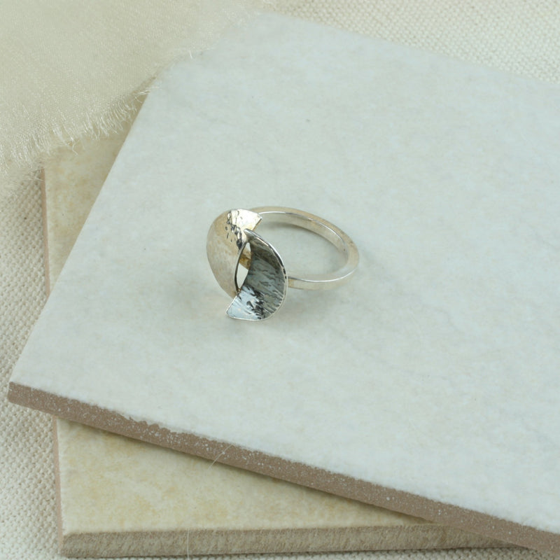 Silver ring featuring a split circle. The band is square and the split circle is a circle which has been sawn in half  and domed. Both sides have been textured and then soldered together in opposite directions. One side is oxidised and has a darker finish.