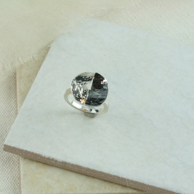 Silver ring featuring a split circle. The band is square and the split circle is a circle which has been sawn in half  and domed. Both sides have been textured and then soldered together in opposite directions. One side is oxidised and has a darker finish.