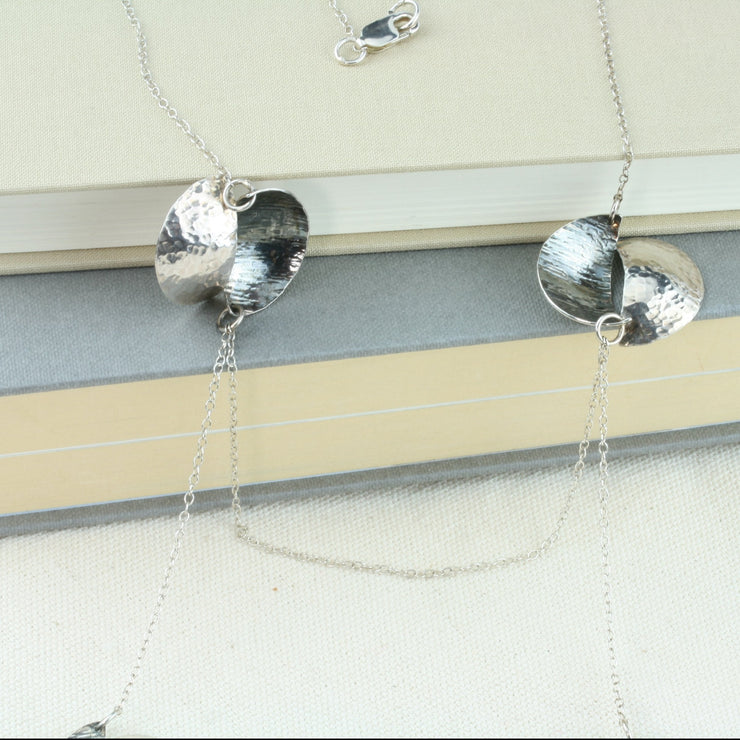 Silver statement necklace with 3 split circles on either side, connectes vertically and horizontally by chain. The  circles are split in half and domed, then soldered together in opposite directions. Both sides have a different hammered texture , one half has a shiny mirror finish, the other an oxidised buffed finish.