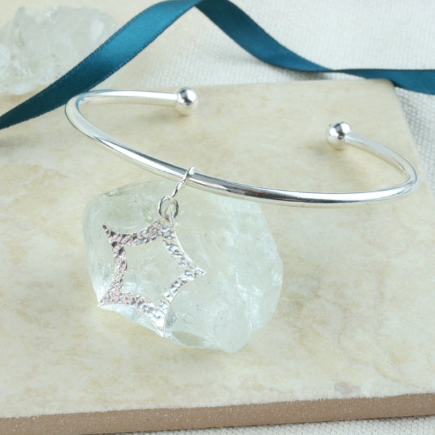 Eco silver bangle bracelet made form round wire 3mm / 0.1" in diameter. With a silver ball on both ends, featuring a star charm of about 20mm / 0.8" in diameter with curved sides and a star opening in the centre.. One side has a hammered texture with a shiny finish, the other a mirror finish.