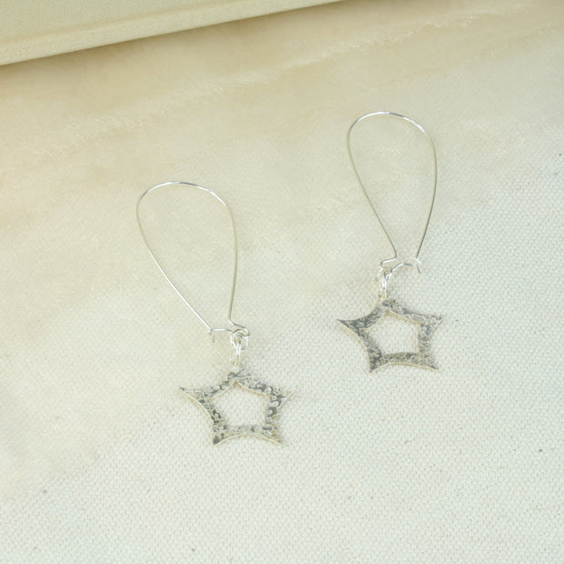 Eco silver long wired earring hooks with a star dangling from the bottom. The front has a hammered shiny finish that sparkles in the light. The back has a mirror finish.