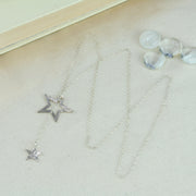 Silver necklace featuring a smaller stars on one end and a larger star on the other. The chain is looped through the larger star. Both stars have a textured finish, the larger star stripes and and the smaller star round dots. Their backs have a mirror finish. By pulling the smaller star through the larger star you can adjust the length.