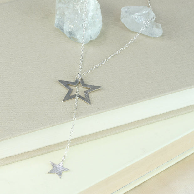 Silver necklace featuring a smaller stars on one end and a larger star on the other. The chain is looped through the larger star. Both stars have a textured finish, the larger star stripes and and the smaller star round dots. Their backs have a mirror finish. By pulling the smaller star through the larger star you can adjust the length.