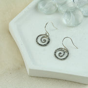 Silver hook earrings featuring a round swirl shape with a hammered texture. 