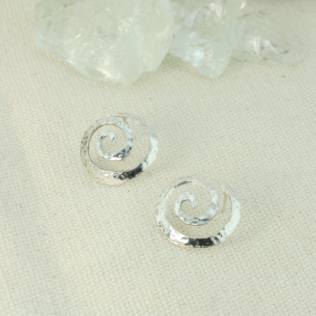 Silver round swirl stud earrings. They have a round hammered texture and shiny finish. The swirls are domed as well.