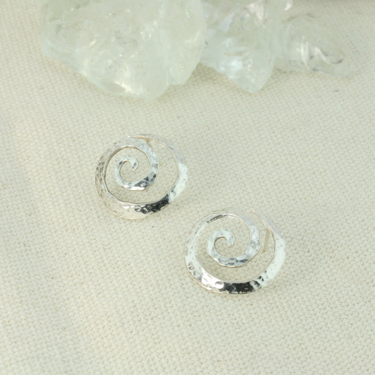 Silver round swirl stud earrings. They have a round hammered texture and shiny finish. The swirls are domed as well.