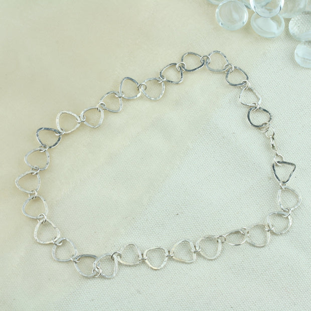 A silver necklace featuring silver triangle shaped links connected by small jump rings. The triangles have a hammered texture which lets the light bounce of f in all directions making it shimmer and sparkle. It&