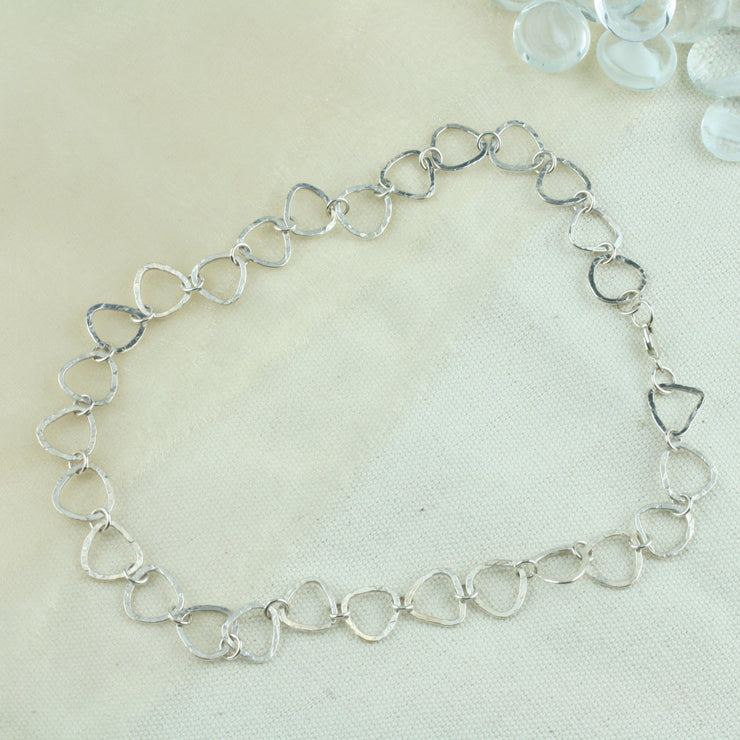 A silver necklace featuring silver triangle shaped links connected by small jump rings. The triangles have a hammered texture which lets the light bounce of f in all directions making it shimmer and sparkle. It&