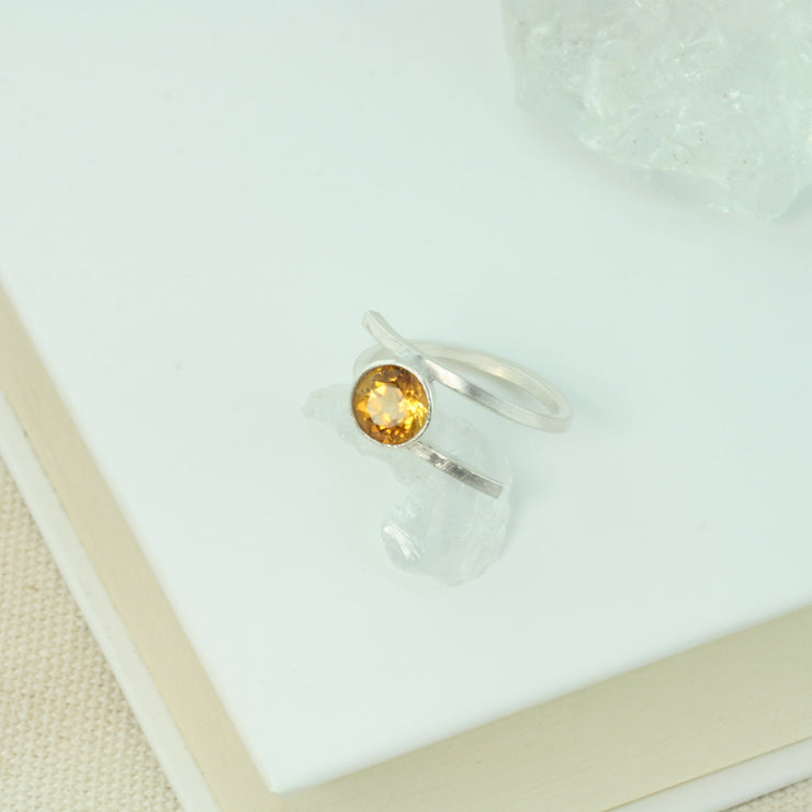 Silver twisted ring made from square eco silver wire. In between the two sides sits a Citrine gemstone in a collet setting. The collet setting raises the gemstone about 10mm above the ring band. The band is adjustable to a few sizes up or down.