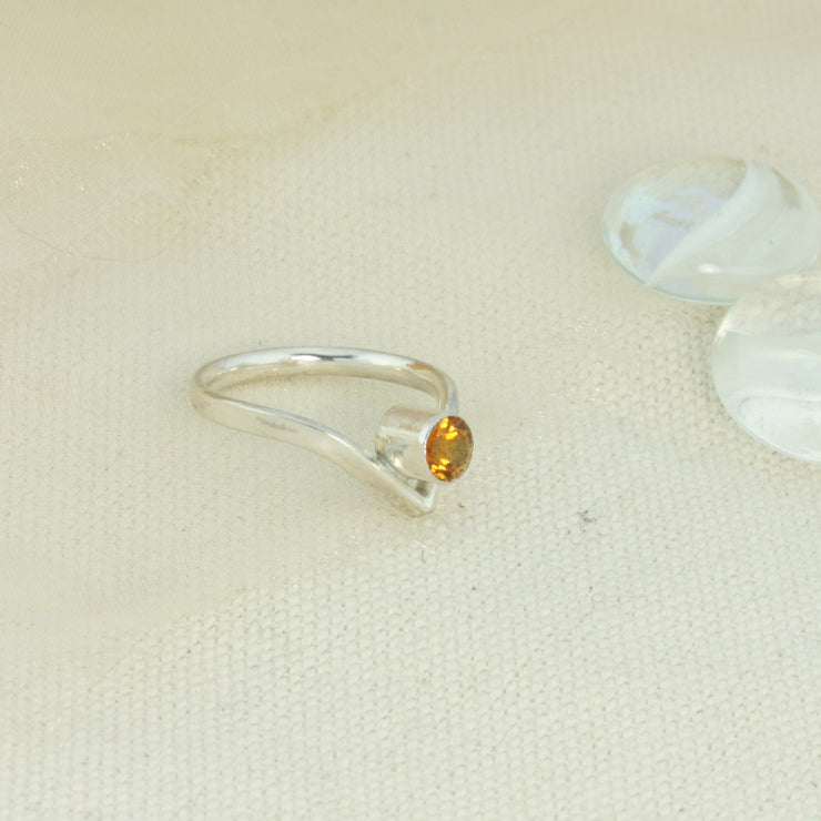 Silver wishbone ring with a Citrine gemstone added to the inside of the dip. The wishbone ring is made from D shaped eco silver wire, with the curve on the inside of the ring band. The wishbone ring is a classic design with a v shaped curve on one side. The curve goes down and the gemstone sits in the curve. This ring features a Citrine gemstone 5mm in diameter set in a tube setting.