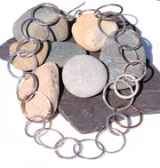 Silver and copper statement necklace featuring hoops in various sizes. All hoops have a hammered texture and shiny finish.  All hoops apart from two near the middle of the necklace are silver, the other two are made from copper.