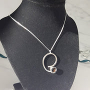 Eco silver swirl pendant with a collet setting held by either end of the swirl. The collet setting features a Smoky Quartz gemstone. The collet setting is open at the back allowing light to fall through and brighten up the gemstone. This has a smoky brown grey colour depending on how it catches the light.