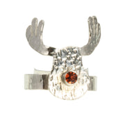 Silver adjustable ring featuring a sawn out Rudolph head. The face has a striped texture and shiny silver finish. The Antlers have a round hammered texture and are aged to give them a darker look, they have been polished to a shine. The red nose is a Garnet gemstone set in a tube setting. The ring band has a striped hammered texture. The ring is adjustable by pinching or pulling the ring band slightly. Matching hook earrings and pendant necklace are available as well.